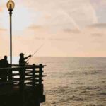 Silhouetted figures fishing on a pier during a breathtaking ocean sunset., tags: wo auf - pexel