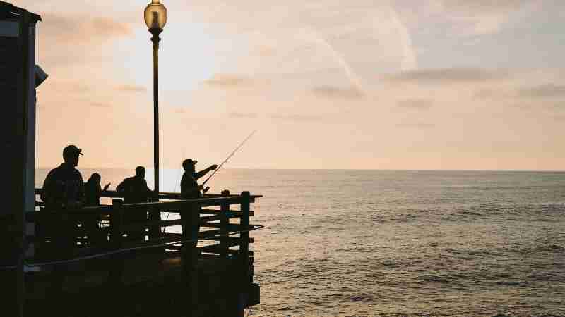 Silhouetted figures fishing on a pier during a breathtaking ocean sunset., tags: wo auf - pexel